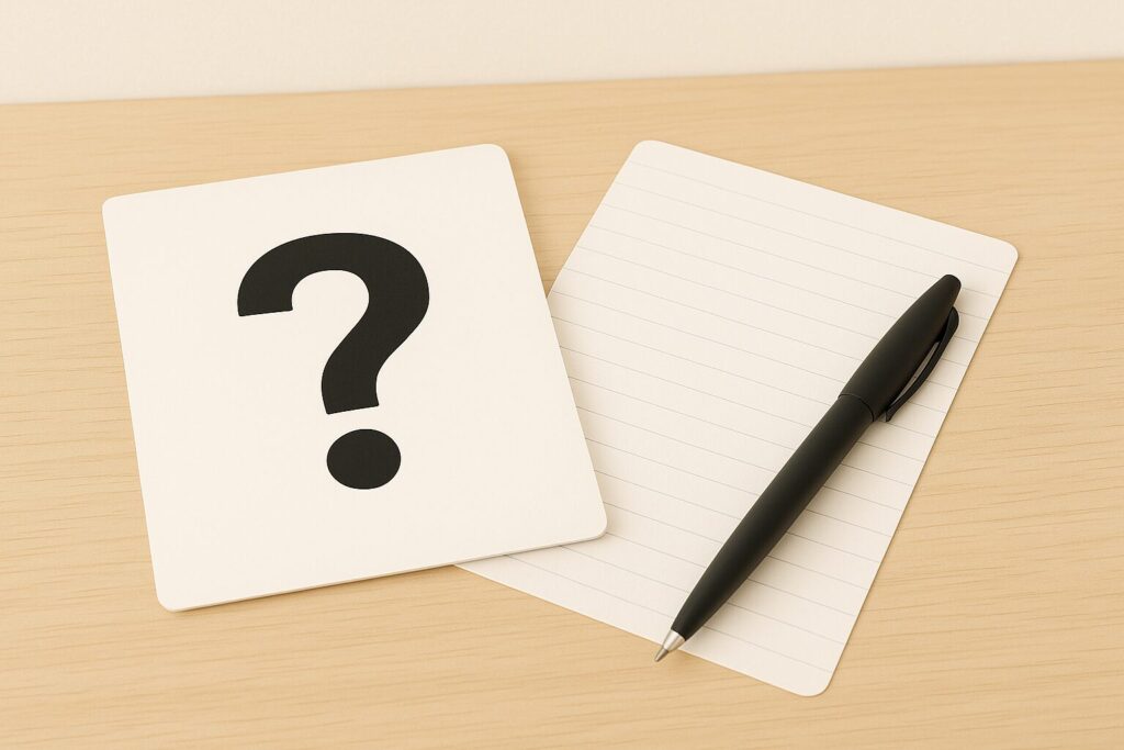 クエスチョンマークが描かれたカードと、横に置かれたペンとメモ用紙が机の上に並んでいる。
